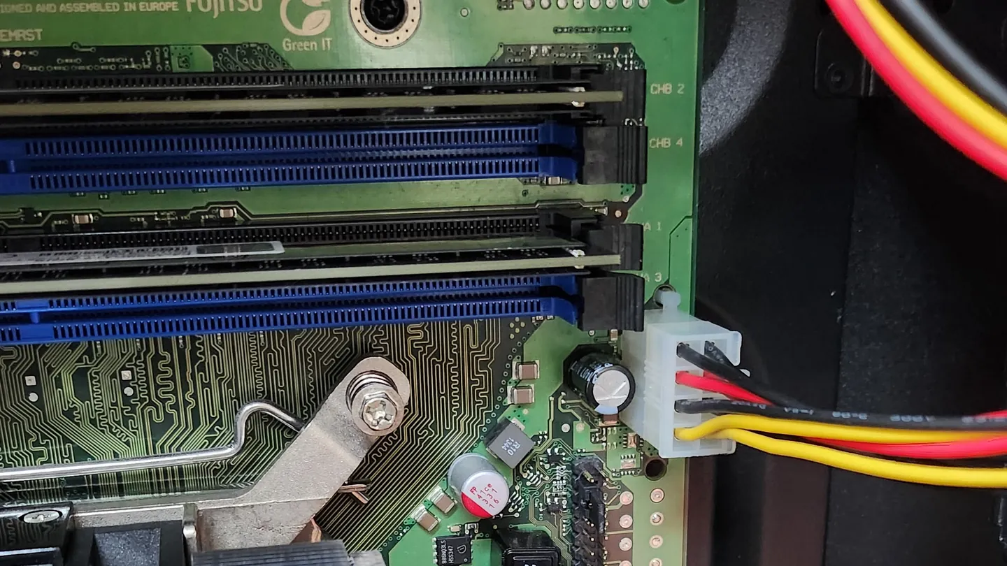 Blick auf eine PC-Hauptplatine mit Arbeitsspeicher-Steckplätzen, Prozessorkühler und Stromkabeln.