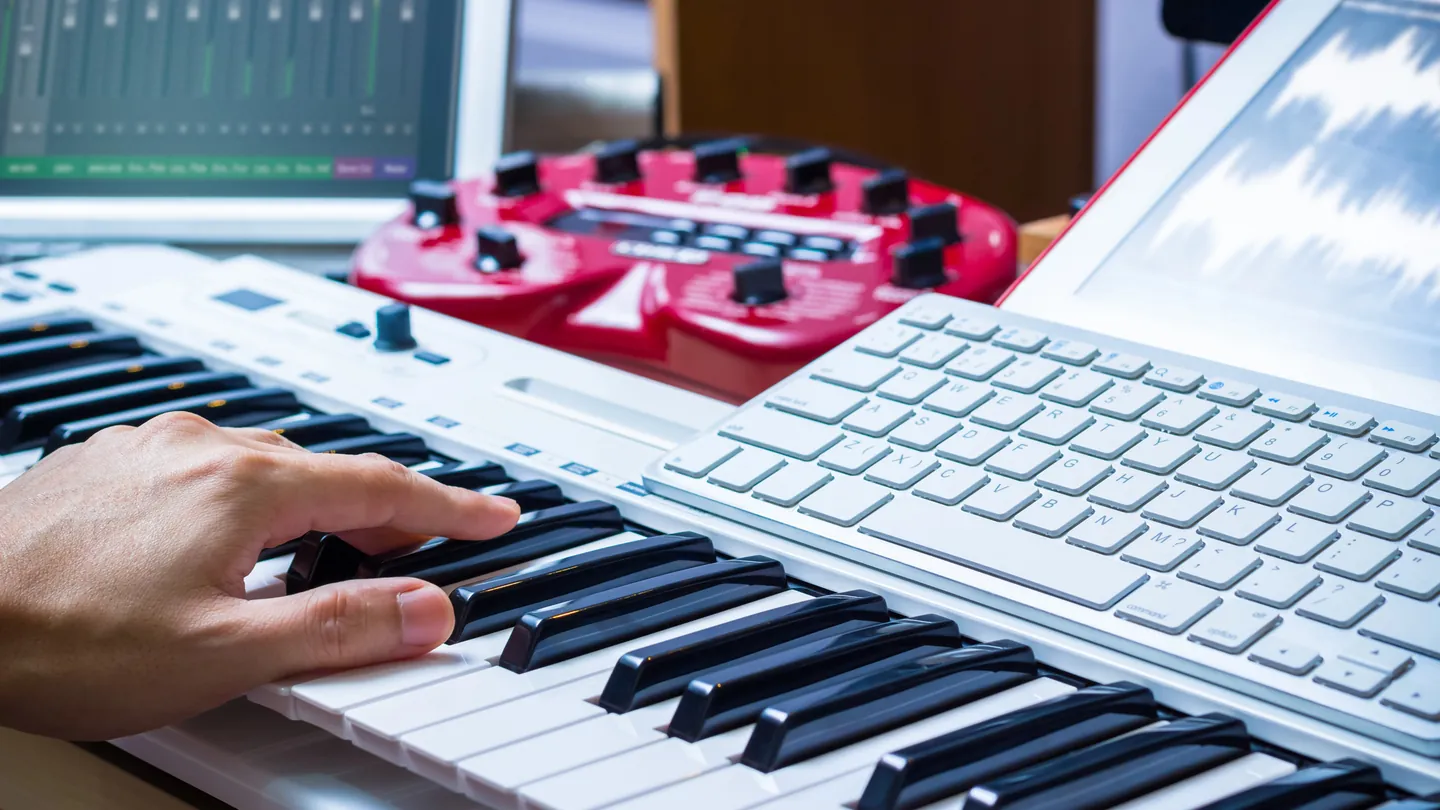 Hände auf einer Klaviertastatur, dahinter ein Mischpult und ein Notebook mit Audioprogramm.