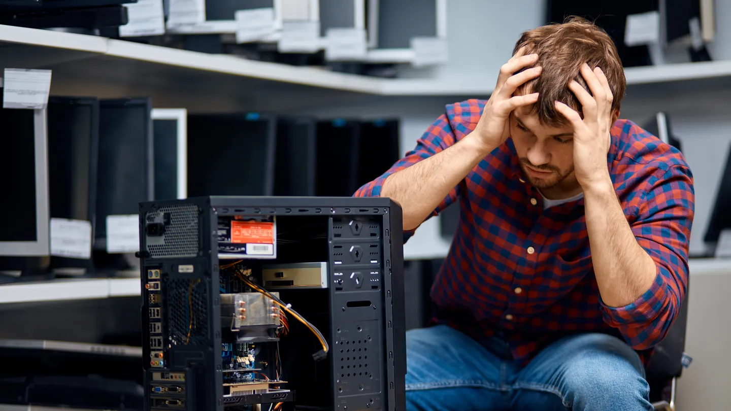Ein Mann sitzt ratlos vor einem geöffneten PC-Gehäuse und hält sich den Kopf.