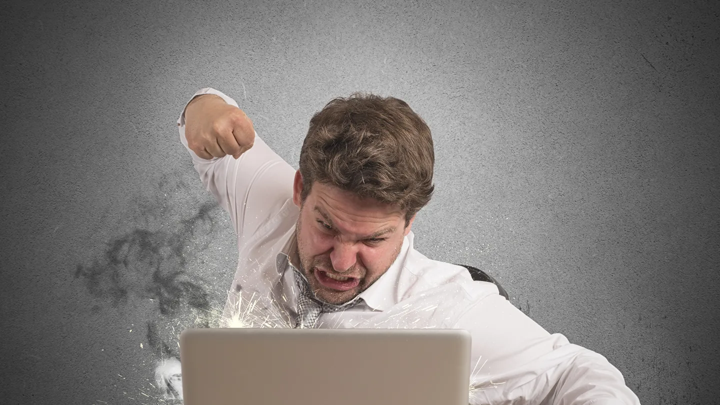 Ein wütender Mann holt mit der Faust über seinem Notebook aus, Rauch steigt auf.