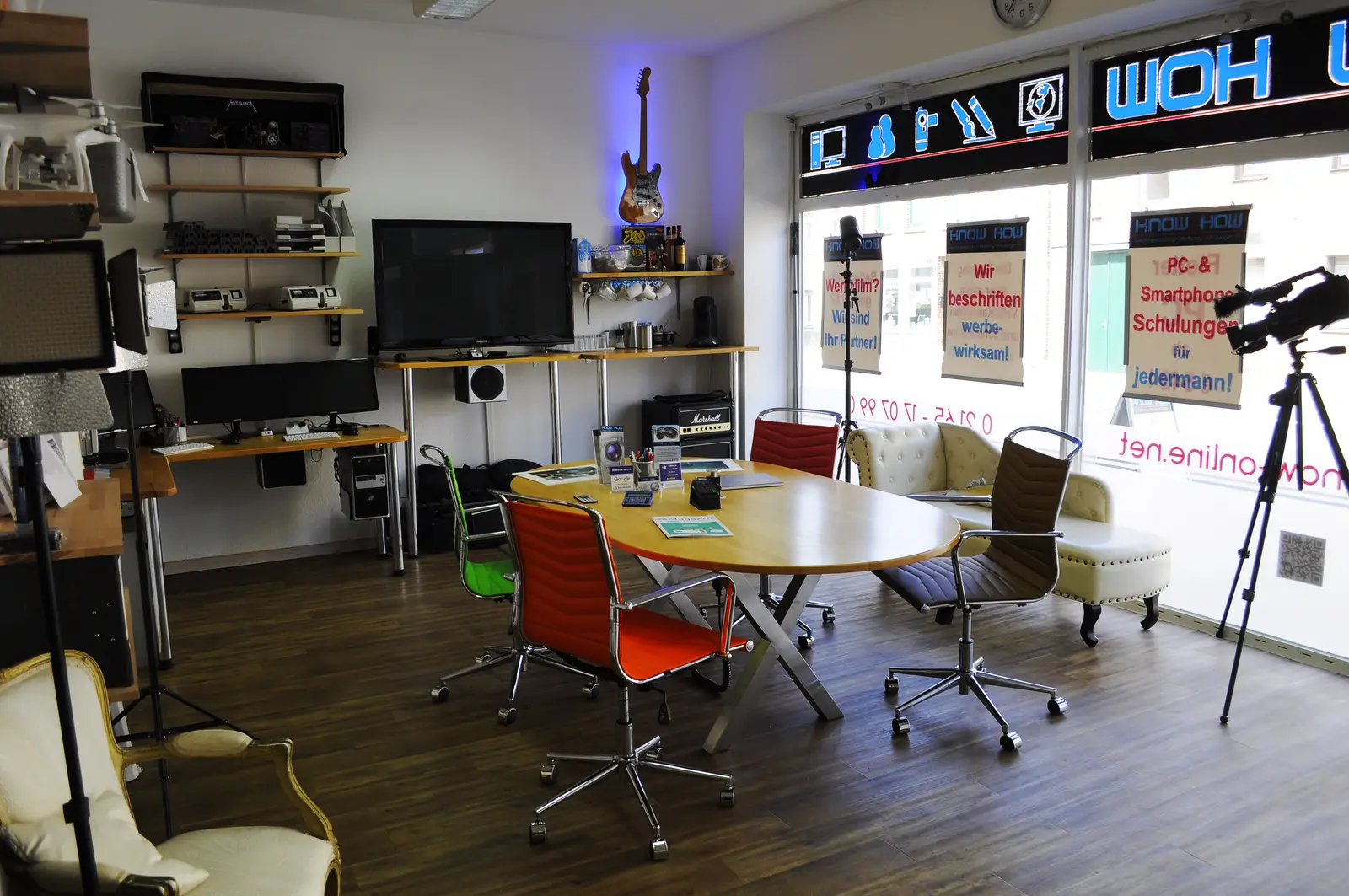Studioausstattung bei KNOW HOW: Kamera auf Stativ, Studioleuchte, Schnittplatz mit zwei Monitoren und Lautsprechern im Beratungsraum.